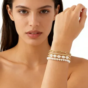 Gros plan détaillé de bracelets empilés en chaîne dorée et perles portés par le modèle.