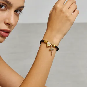 Dettaglio bracciale cordino nero con ciondolo lettera cuore e croce in zirconi.