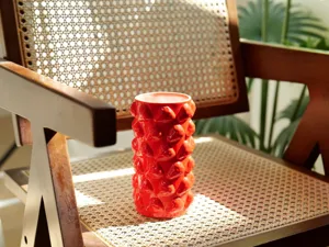 Detailaufnahme der roten Keramikvase mit strukturierter Zylinderform und plastischem Fruchtdekor.
