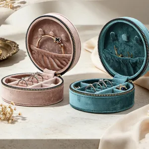 Detailed view of open velvet round jewelry boxes in pink and teal showing internal storage
