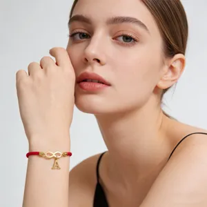 Close-up detail shot of red woven string bracelet with gold letter A pendant and infinity charm.