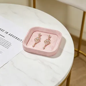 Roze fluwelen sieradentray op marmeren tafel met gouden oorbellen.