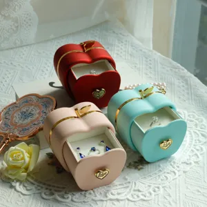 Close-up of apple-shaped jewelry gift boxes in red, pink, and blue with rings inside