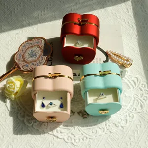 Detailed view of apple-shaped jewelry boxes in red, pink, and mint green with jewelry inside.