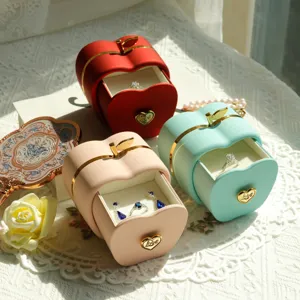 Detail of matte apple-shaped jewelry gift boxes in red, green, and pink with gold accents.
