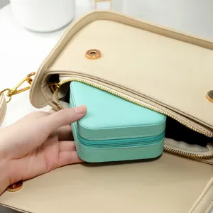 Portable mint green heart-shaped travel jewelry box being placed inside a stylish handbag.