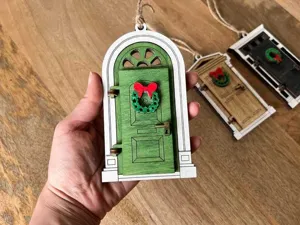 Wooden miniature fairy door ornament with wreath for garden tree hanging decor and display.