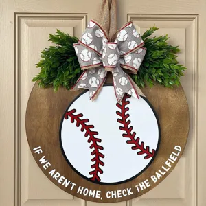 Wooden baseball door hanger detail, round door sign with bow and greenery for front porch decor.