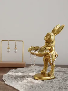 Macro detail of a vintage golden rabbit figurine holding a shell-shaped jewelry display tray.