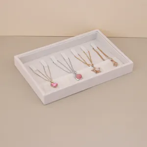 Light gray suede jewelry display tray organizing necklaces on a neutral beige background