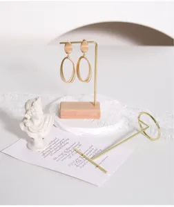 Detalle de un soporte de joyería minimalista en metal dorado con una base de madera natural