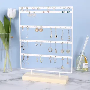 White iron jewelry rack with four tiers and wood base showing various earrings.