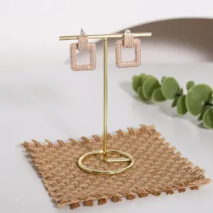 Elegante soporte metálico dorado para pendientes en barra T sobre alfombra tejida rústica