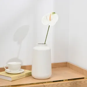 Detail view of a white ceramic vase with an artificial anthurium flower for home decor.