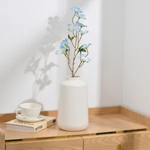 Vue rapprochée de délicates fleurs artificielles en soie bleue dans un vase en céramique blanche.