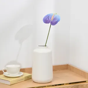 Close-up detail of artificial purple anthurium flower in minimalist white ceramic vase.