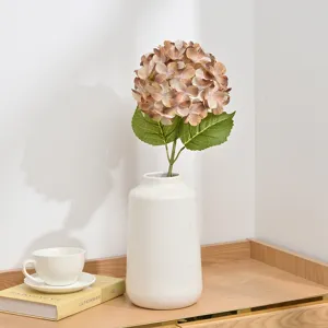 Artificial hydrangea flower arrangement in white ceramic vase home decor detail view.