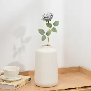 Künstliche kurze Rosenblüte mit weißer Keramikvase für Schreibtischdekoration und Fotorequisite.