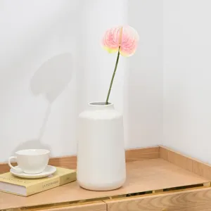 Artificial pink anthurium flower in a modern white ceramic vase for home decor detail view.