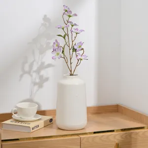 Vue détaillée de branches de fleurs artificielles lilas prunier dans un vase en céramique blanche.