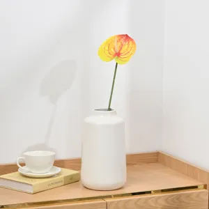 Detail shot of artificial anthurium flower in white ceramic vase on wooden table setup.