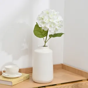 Artificial white hydrangea flower arrangement in ceramic vase, elegant home decor detail shot.