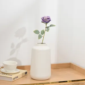 Künstliche violette Rosenblüte mit weißer Keramikvase für die Tischdekoration zu Hause.