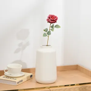 Detailansicht einer künstlichen kurzen Rosenblüte in weißer Keramikvase auf dem Tisch.
