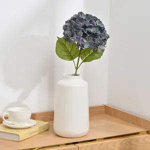 Artificial hydrangea flower in white ceramic vase with green leaves for home decoration.