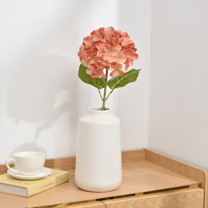 Detailed view of artificial hydrangea flower in white ceramic vase on wooden desktop setup.