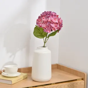 Detailed close-up view of a pink artificial hydrangea flower branch in a white vase setup.