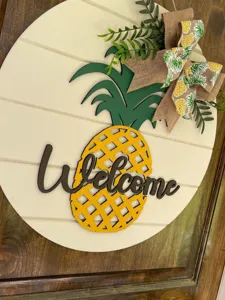 Nahaufnahme eines hölzernen Ananas-Willkommensschildes mit Juteschleife und grünen Blättern.