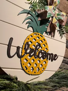 Nahaufnahme des hölzernen Ananas Willkommensschildes mit dekorativer Schleife und Text.