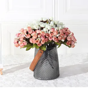 Künstlicher Blumenstrauß mit kleinen Rosenknospen in grauer Glasvase für Heimdekoration.