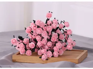 Nahaufnahme künstlicher rosa Schaumstoffrosen mit schwarzen Stielen auf einem Holztablett.