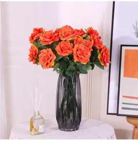 Detailaufnahme künstlicher orangefarbener Rosen in gerippter grauer Glasvase für Deko.