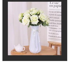Detailansicht eines künstlichen weißen Rosenstrauchs in einer modernen weißen Vase auf Holz.