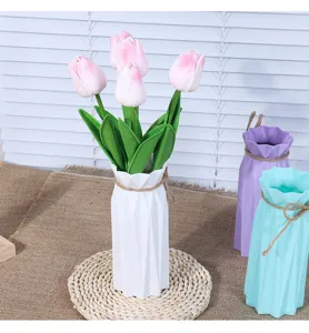Detail view of the modern minimalist plastic vase with artificial pink tulips and green leaves.