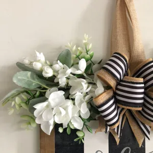 Dettaglio insegna in legno, ghirlanda rustica con fiocco a righe bianche e nere e fiori.
