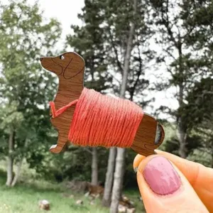 Close-up detail view of the charming wooden dachshund floss bobbin wrapped with bright orange thread.