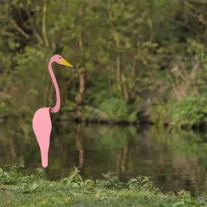 Stylish metal pink flamingo garden ornament stake standing by a natural riverside pond
