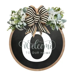 Dettaglio cartello porta rotondo in legno con fiocco bianco nero, verde e testo di benvenuto.
