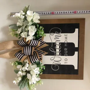 Dettaglio insegna porta benvenuto in legno con fiocco floreale e lettera H rustica.