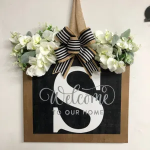 Targa per porta in legno rustico con lettera S, testo di benvenuto e fiori artificiali.