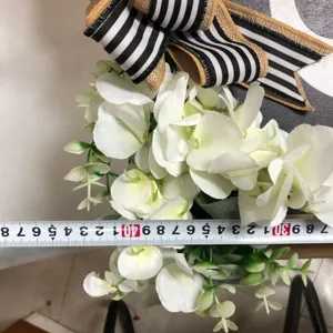 Bouquet di fiori bianchi artificiali con fiocco a righe e dettaglio di nastro di misura.