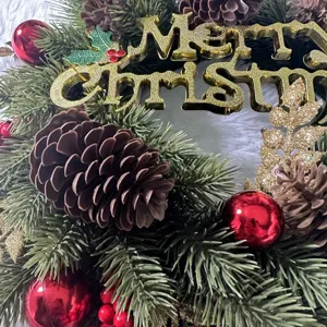 Nahaufnahme eines künstlichen Weihnachtskranzes mit Zapfen und goldenem Merry-Christmas-Schild.