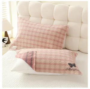 Détail de taie d'oreiller en gaze à carreaux rose montrant un tissu coton doux et broderie papillon.