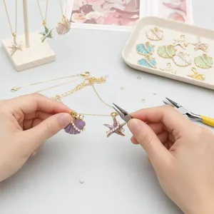 Hands using pliers to assemble a colorful starfish pendant on a gold necklace chain