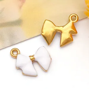 Detalle de dijes de lazo de esmalte blanco y acero inoxidable dorado para creación de joyería.
