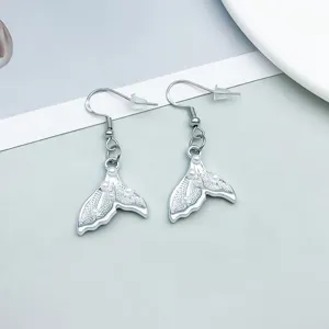 Close-up detail of silver mermaid tail earrings decorated with white pearls and engraving.
